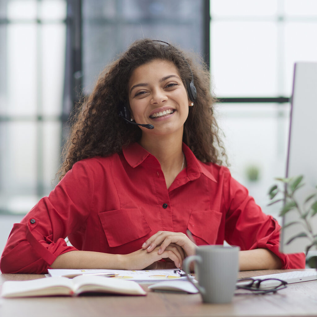 A,Young,Attractive,Woman,In,A,Red,Shirt,Sits,At A young attractive woman in a red shirt sits at a table in a red jacket in headphones with a microphone.